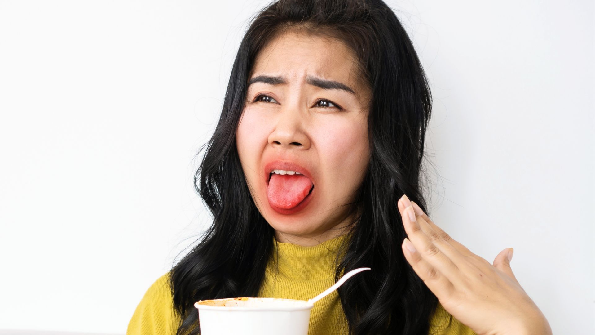 Woman sticking out her tongue and fanning her mouth while holding a cup, illustrating dry mouth and oral discomfort during menopause.