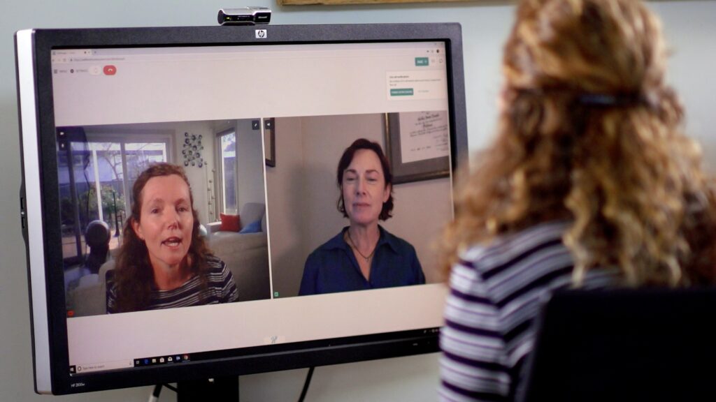Woman watching a video call on her computer screen, reflecting on WellFemme’s first year of online consultations and connection.