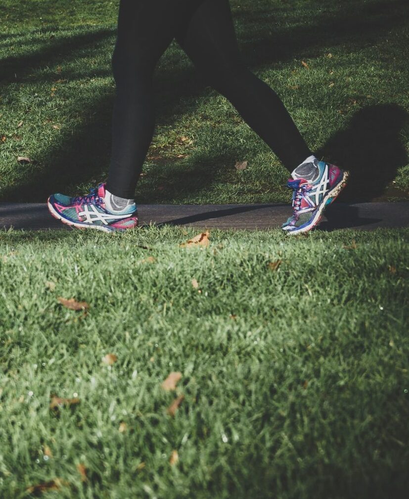 Woman walking outdoors on grass in colourful trainers, representing gentle exercise to help combat low energy during menopause.