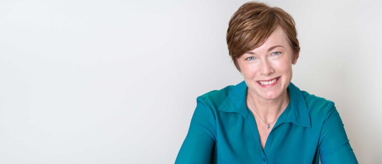 Confident woman in a teal blouse smiling at the camera, representing supportive advice for perimenopausal women.