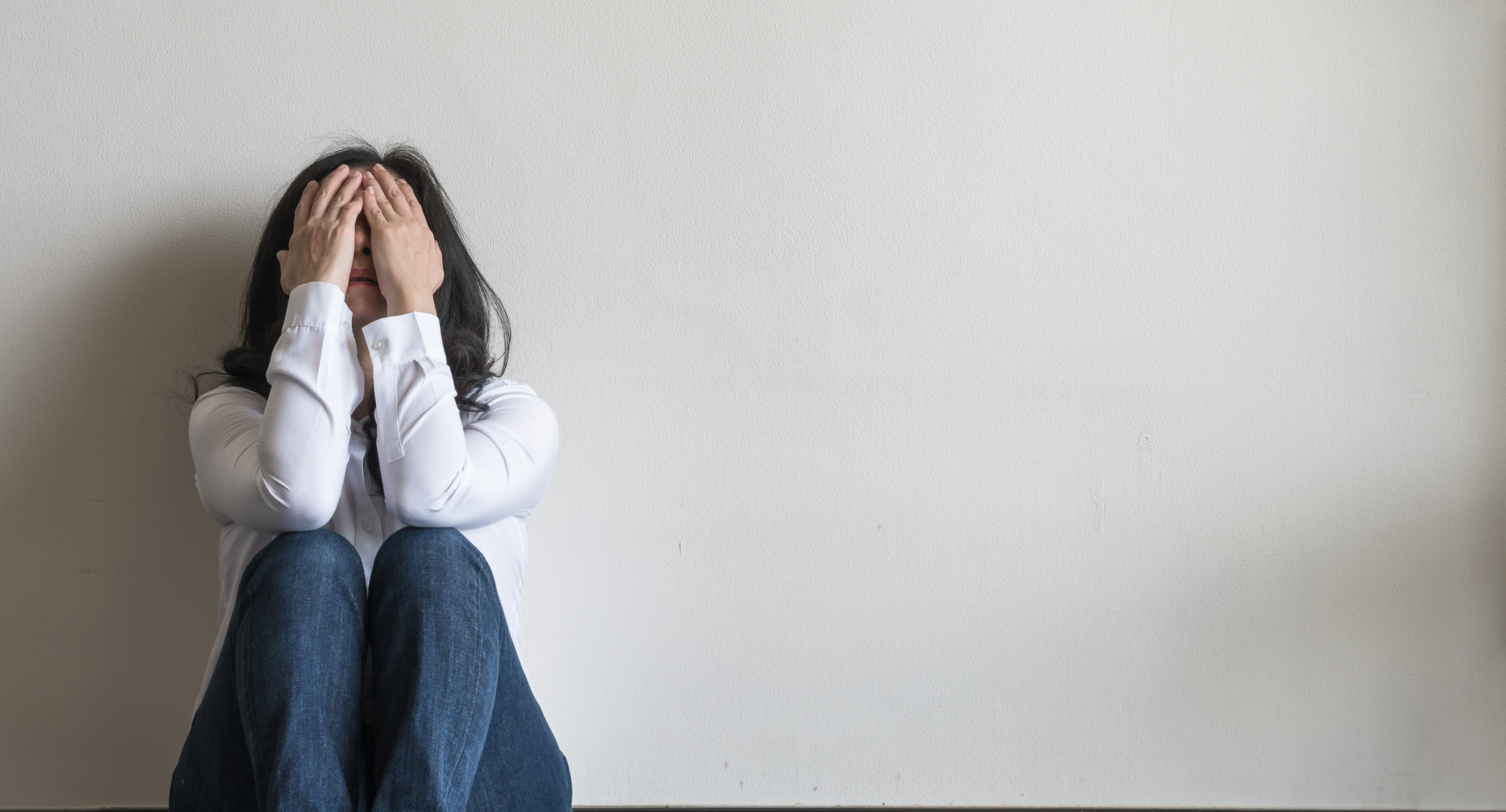 Woman sitting on the floor with her head in her hands, illustrating emotional distress linked to mental health and menopause.