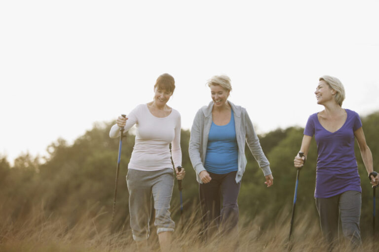 Three middle-aged women walking together outdoors with Nordic walking poles, reflecting shared conversations and experiences about menopause