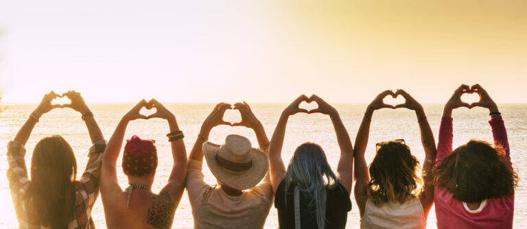 Group of women standing together at sunset with arms raised in heart shapes, symbolising solidarity and finding peace after a difficult endometriosis and HRT journey.