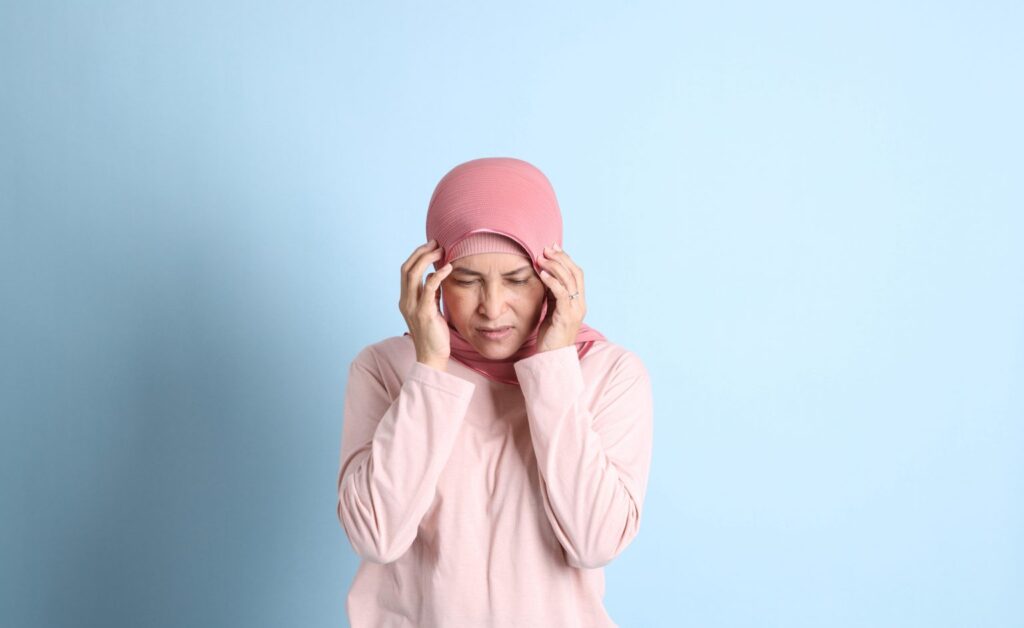 Woman in pink holding her temples with eyes closed, illustrating migraine pain during perimenopause and menopause.