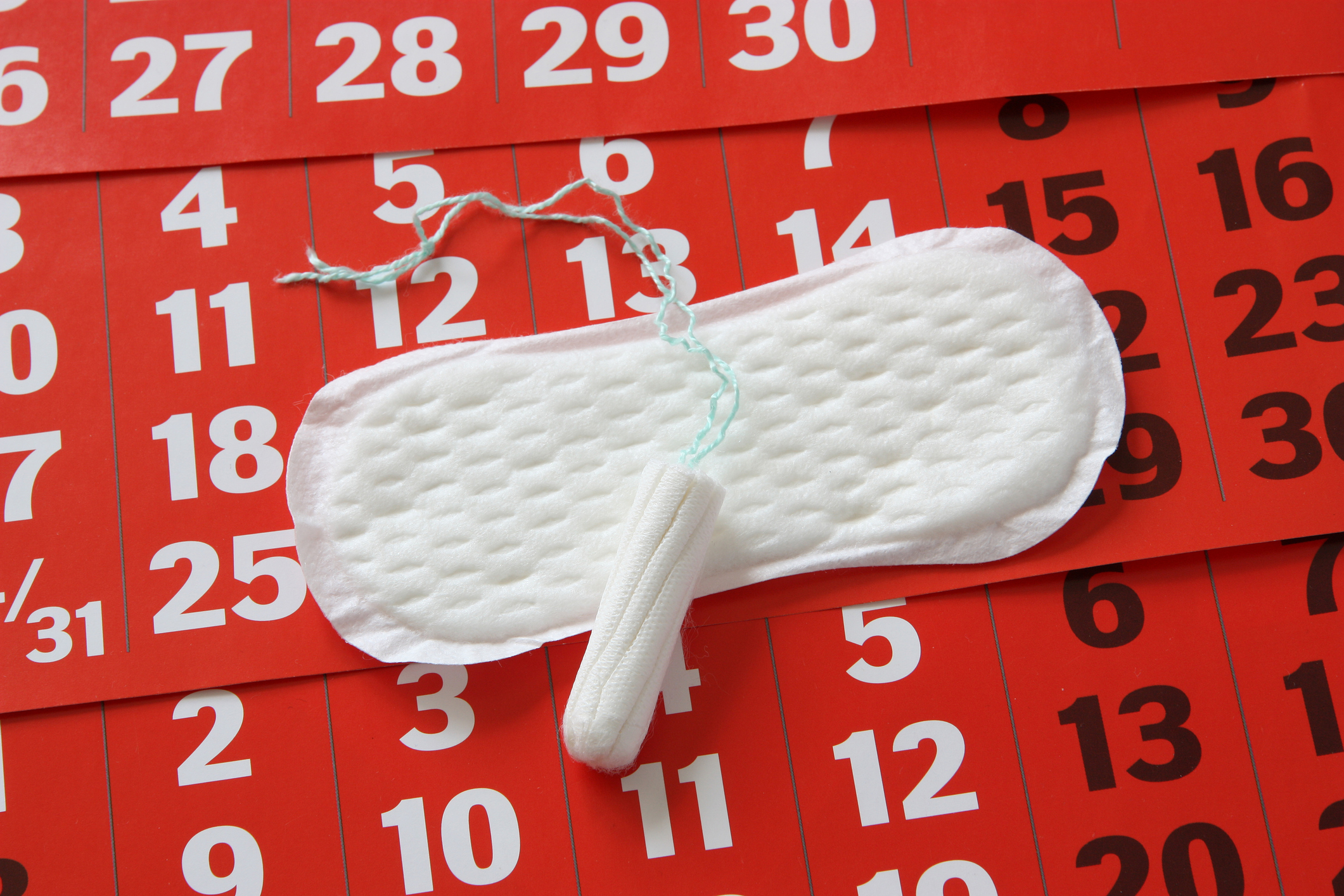A sanitary pad and tampon placed on a red calendar, illustrating common period problems and menstrual cycle planning.
