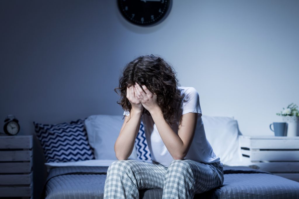 Exhausted woman sitting on a sofa at night with her head in her hands, illustrating fatigue and emotional overwhelm linked to burnout and menopause.