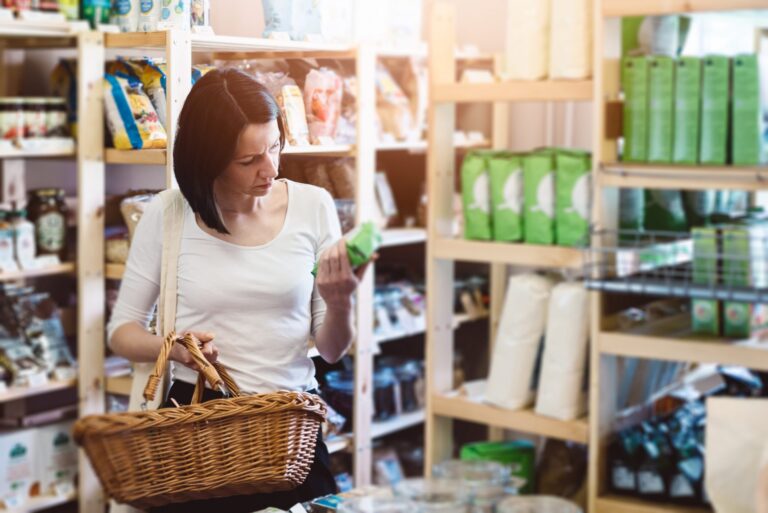 Woman in a health shop reading the label on a supplement bottle, representing choosing supplements for sleep, hot flushes and breast pain during menopause.