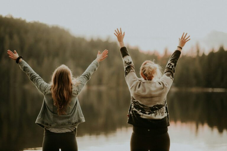 Two women standing by a calm lake with their arms raised, symbolising hope and positive change in menopause care following new government promises.